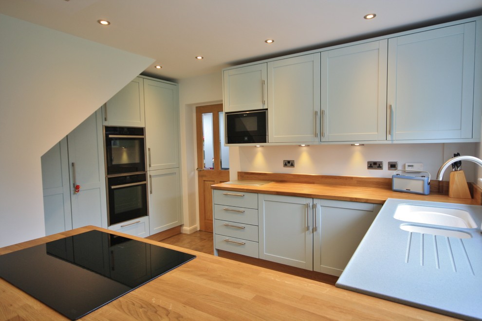 Immagine di una grande cucina ad ambiente unico contemporanea con lavello integrato, ante in stile shaker, ante blu, top in legno e elettrodomestici neri