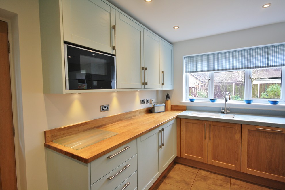 Foto di una grande cucina ad ambiente unico minimal con lavello integrato, ante in stile shaker, ante blu, top in legno e elettrodomestici neri