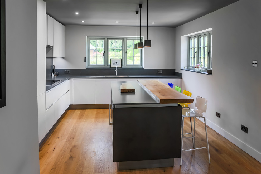 Medium sized contemporary l-shaped open plan kitchen in Essex with an integrated sink, flat-panel cabinets, grey cabinets, quartz worktops, grey splashback, stone slab splashback, integrated appliances, medium hardwood flooring, an island, multi-coloured floors and grey worktops.