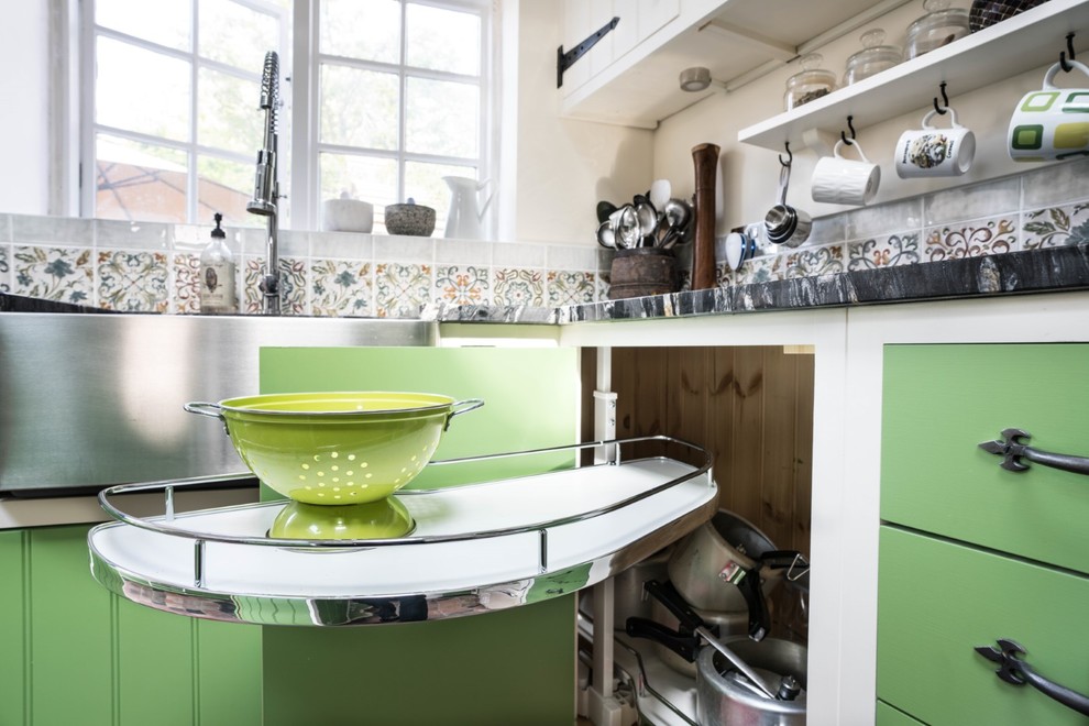 Photo of a small rural l-shaped kitchen/diner in Essex with a belfast sink, green cabinets, granite worktops, multi-coloured splashback, mosaic tiled splashback, integrated appliances, porcelain flooring, an island, multi-coloured floors and black worktops.