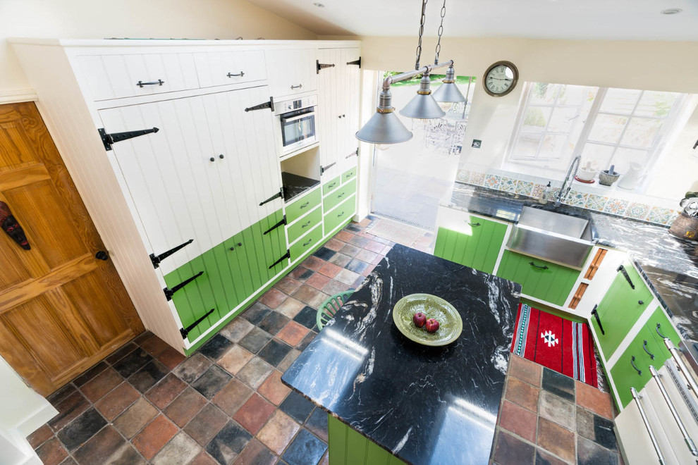 Lantlig inredning av ett litet svart svart kök, med en rustik diskho, gröna skåp, granitbänkskiva, flerfärgad stänkskydd, stänkskydd i mosaik, integrerade vitvaror, klinkergolv i porslin, en köksö och flerfärgat golv