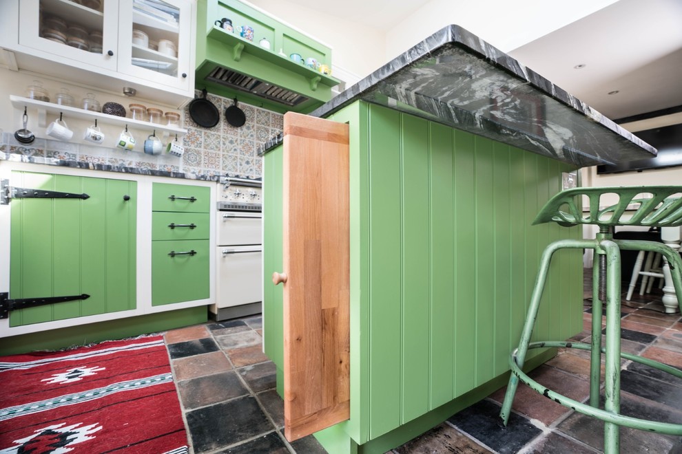Inspiration for a small farmhouse l-shaped kitchen/diner in Essex with a belfast sink, green cabinets, granite worktops, multi-coloured splashback, mosaic tiled splashback, integrated appliances, porcelain flooring, an island, multi-coloured floors and black worktops.
