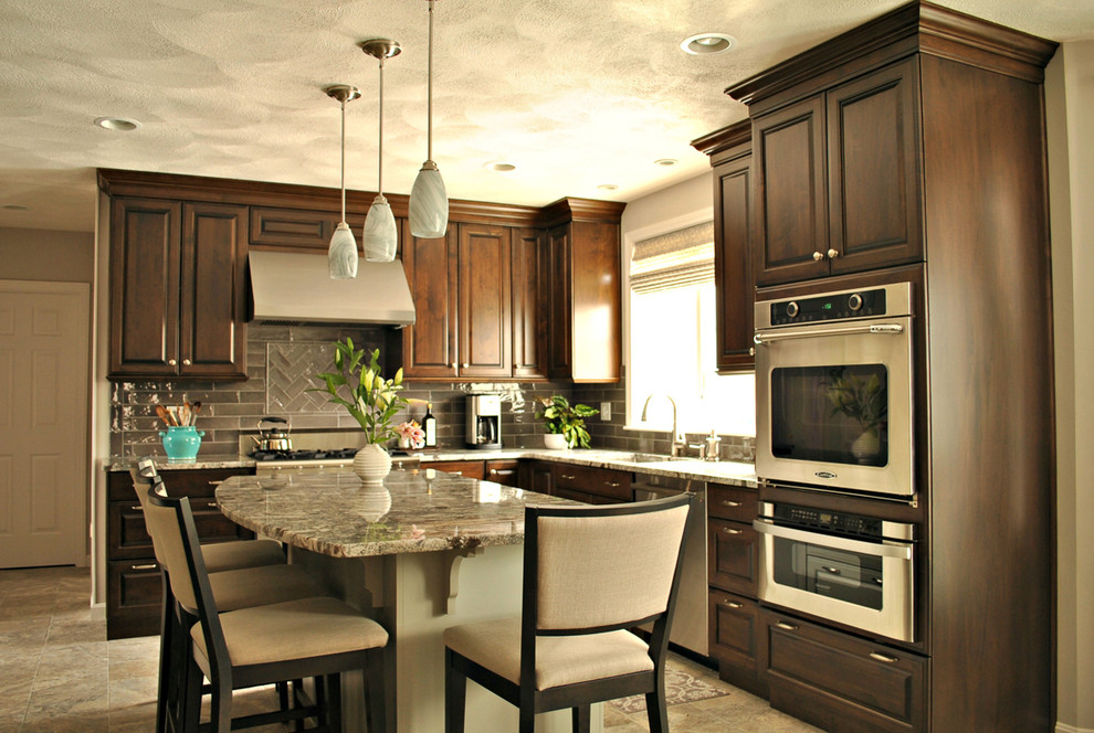Foto på ett mellanstort vintage kök, med en undermonterad diskho, luckor med upphöjd panel, skåp i mörkt trä, granitbänkskiva, grått stänkskydd, stänkskydd i glaskakel, rostfria vitvaror och en köksö