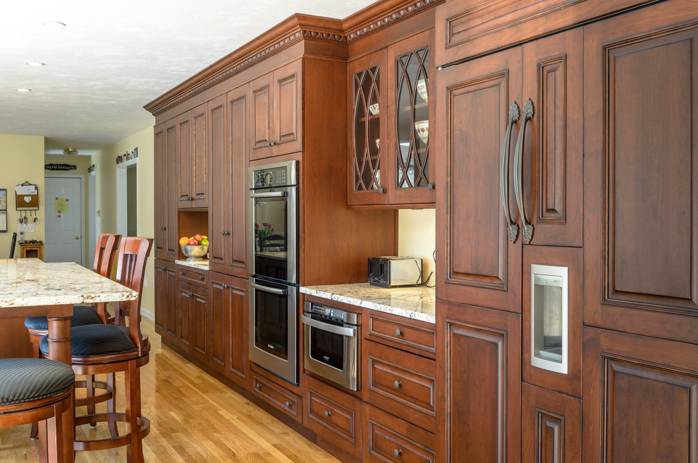 Klassisk inredning av ett kök, med en undermonterad diskho, luckor med upphöjd panel, bruna skåp, granitbänkskiva och rostfria vitvaror