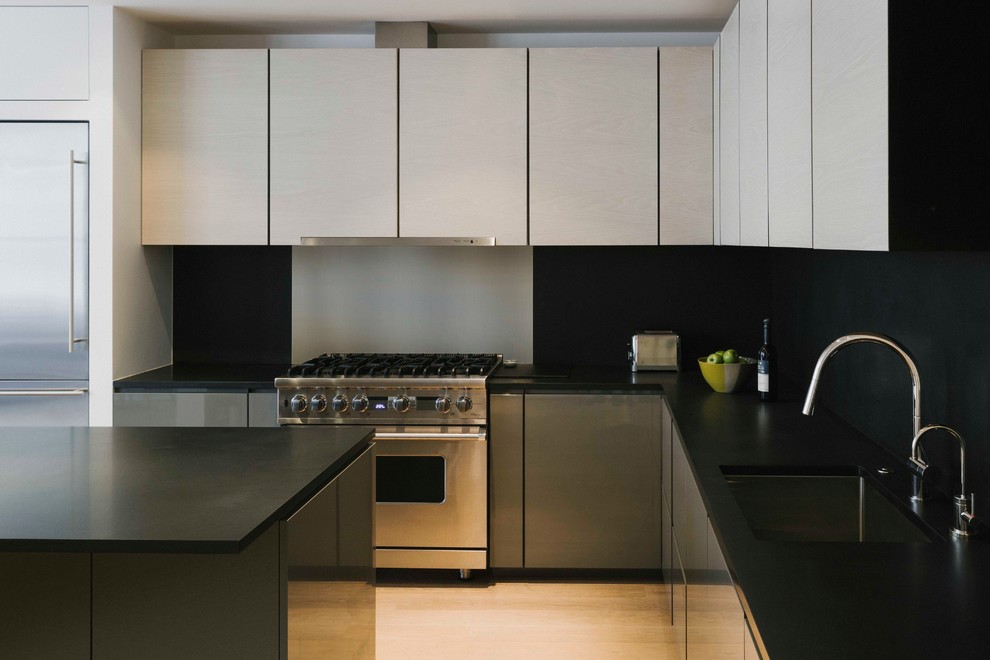 Immagine di una cucina minimalista di medie dimensioni con lavello sottopiano, ante grigie, top in superficie solida, paraspruzzi nero, elettrodomestici in acciaio inossidabile e parquet chiaro