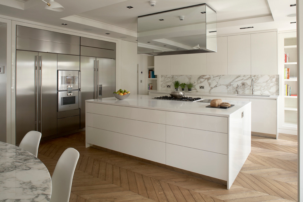 Photo of a contemporary kitchen in London with flat-panel cabinets, white cabinets, white splashback, stainless steel appliances and marble splashback.