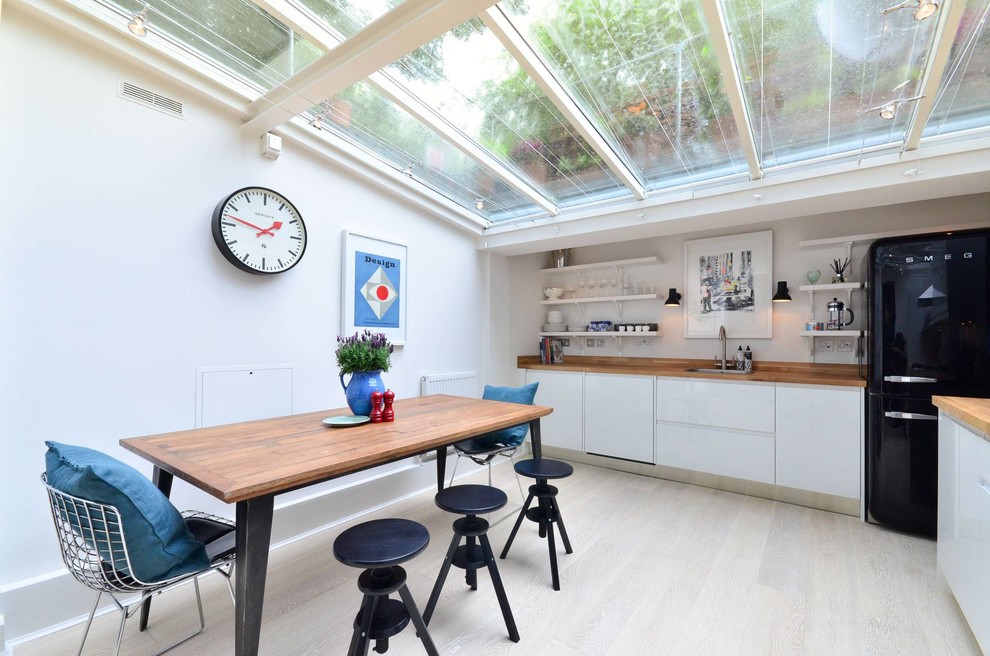 Contemporary l-shaped kitchen in London with a submerged sink, flat-panel cabinets, white cabinets, wood worktops, black appliances and an island.