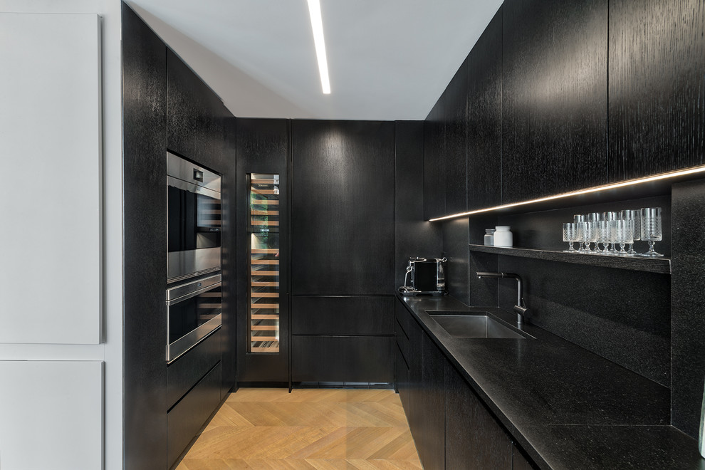 Esempio di una piccola cucina parallela design chiusa con lavello sottopiano, ante nere, top in granito, paraspruzzi nero, elettrodomestici neri, pavimento in legno massello medio, pavimento marrone e top nero