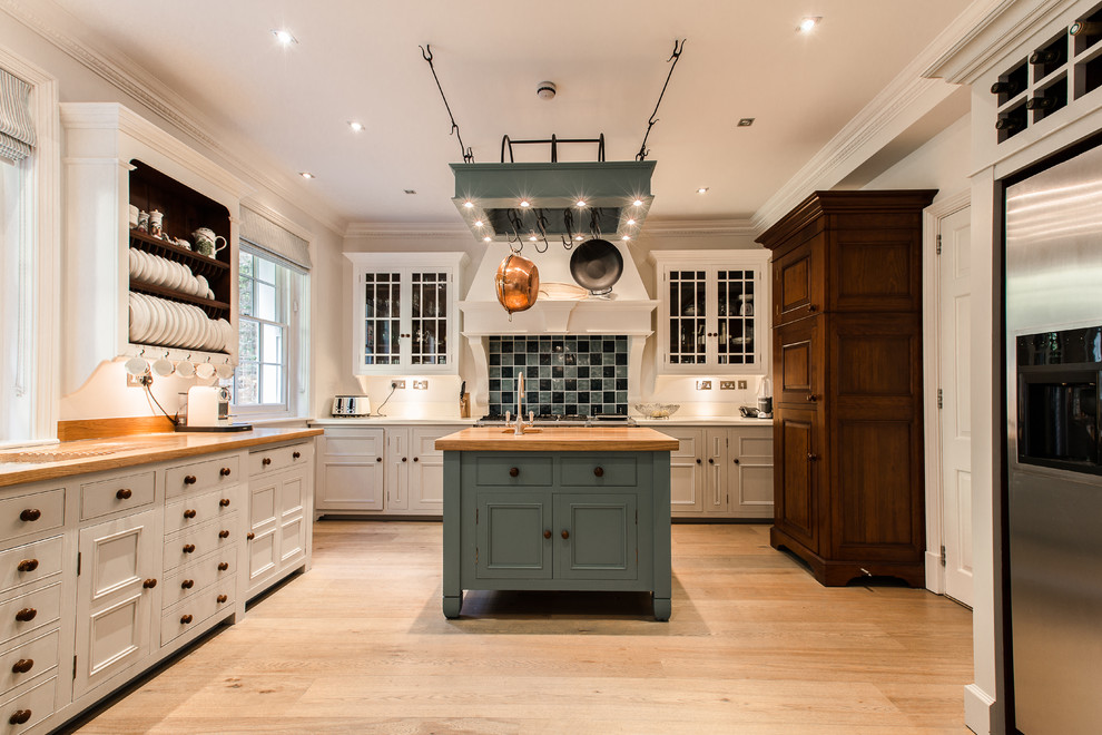 Klassische Küche mit Kassettenfronten, weißen Schränken, Arbeitsplatte aus Holz, bunter Rückwand, Küchengeräten aus Edelstahl, hellem Holzboden und Kücheninsel in London