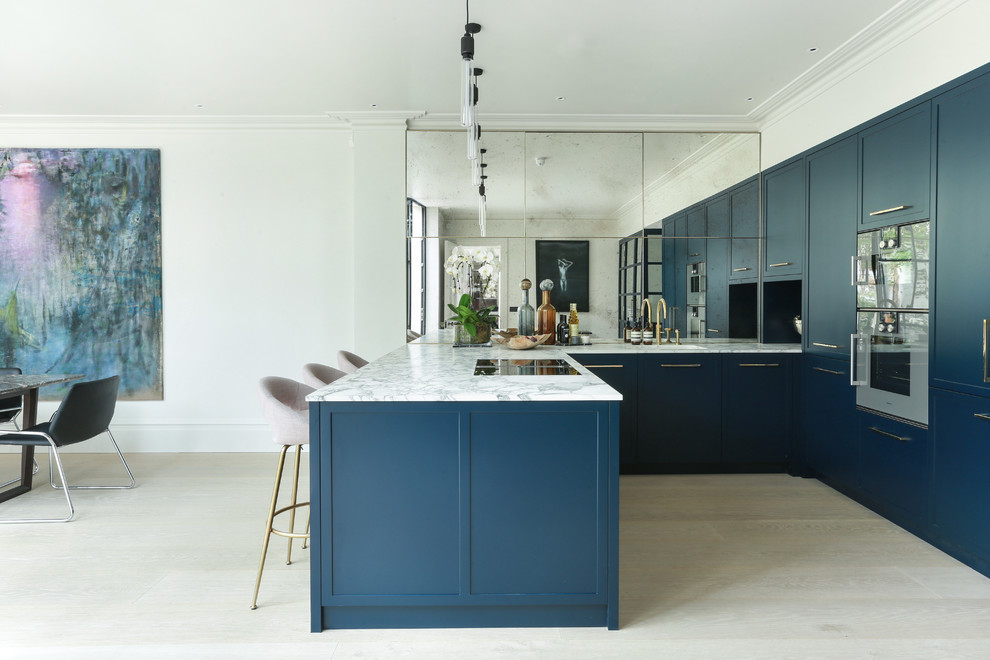 Inspiration for a contemporary u-shaped kitchen/diner in London with a submerged sink, shaker cabinets, blue cabinets, metallic splashback, mirror splashback, stainless steel appliances, light hardwood flooring, a breakfast bar, beige floors and white worktops.