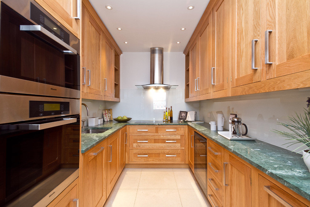 This is an example of a contemporary enclosed kitchen in London with stainless steel appliances, a single-bowl sink, shaker cabinets, medium wood cabinets, white splashback and glass sheet splashback.