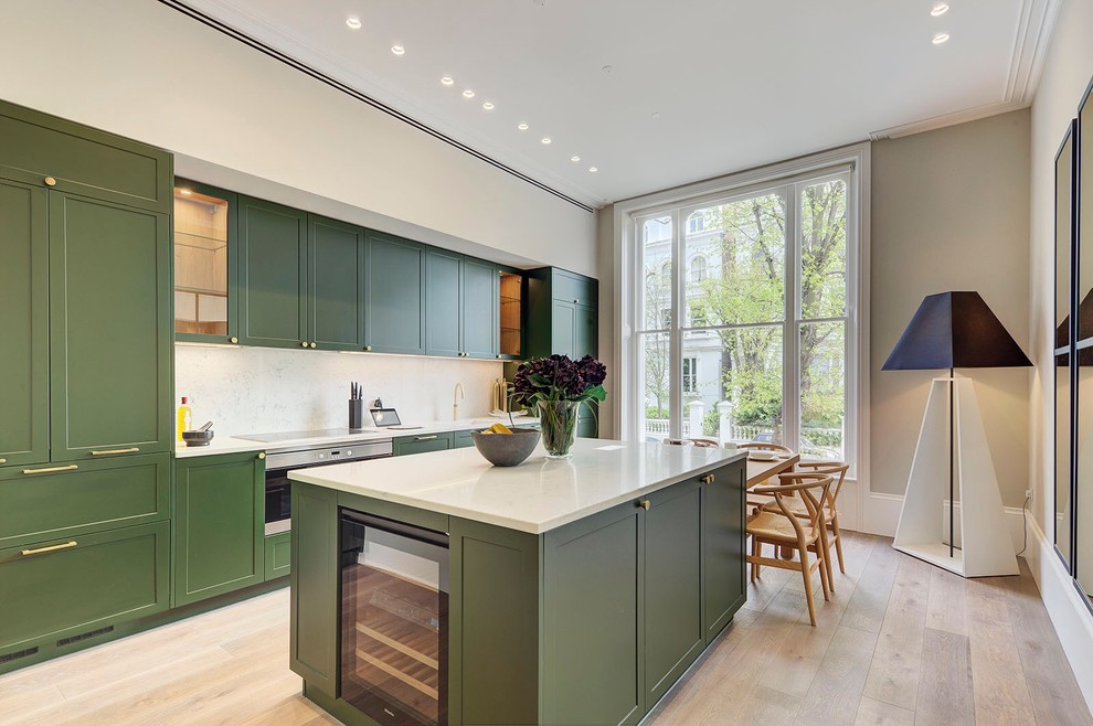 Example of a mid-sized transitional single-wall light wood floor and beige floor eat-in kitchen design in London with an island, green cabinets, white backsplash, marble backsplash, stainless steel appliances, white countertops and shaker cabinets