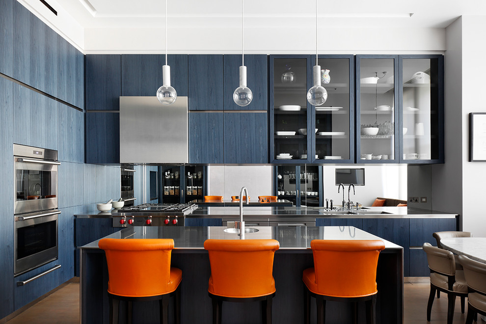 Cette image montre une cuisine américaine design en L avec un évier intégré, un placard à porte plane, des portes de placard bleues, une crédence miroir, un électroménager en acier inoxydable et îlot.