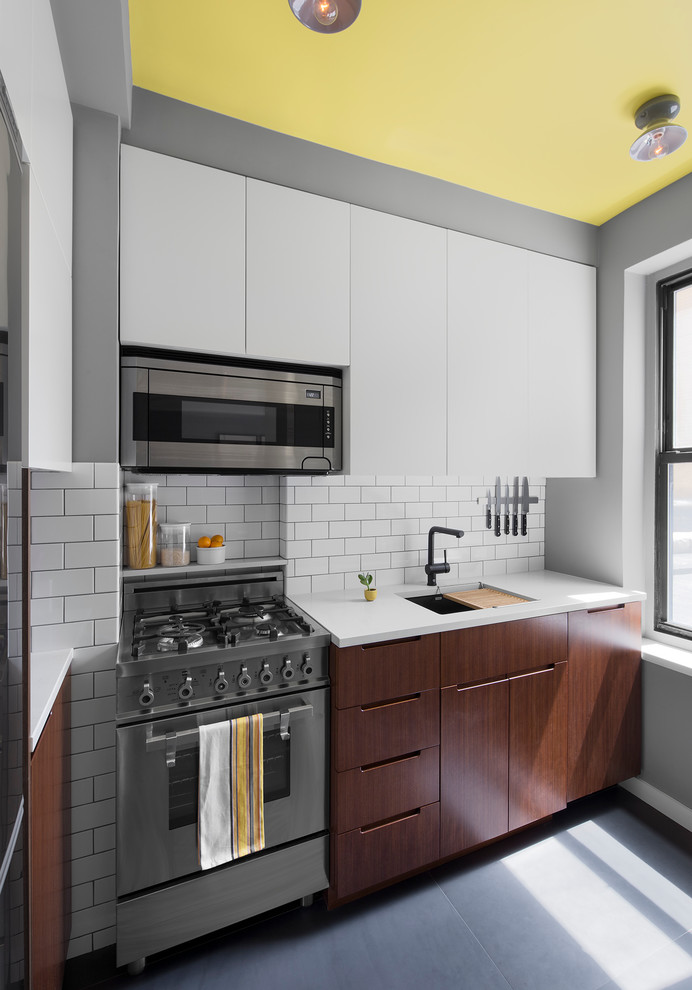 ニューヨークにあるお手頃価格の小さなコンテンポラリースタイルのおしゃれなキッチン (フラットパネル扉のキャビネット、白いキッチンパネル、セラミックタイルのキッチンパネル、アンダーカウンターシンク、濃色木目調キャビネット、人工大理石カウンター、シルバーの調理設備、コンクリートの床、アイランドなし) の写真