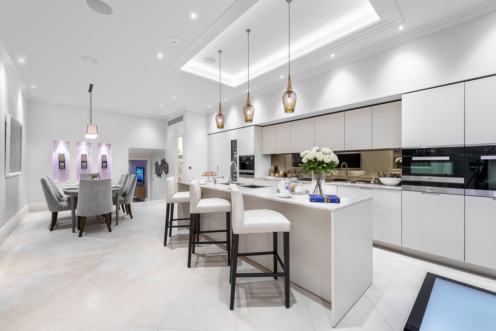 Large modern galley kitchen/diner with a double-bowl sink, flat-panel cabinets, grey cabinets, mirror splashback, black appliances, an island, grey floors and grey worktops.