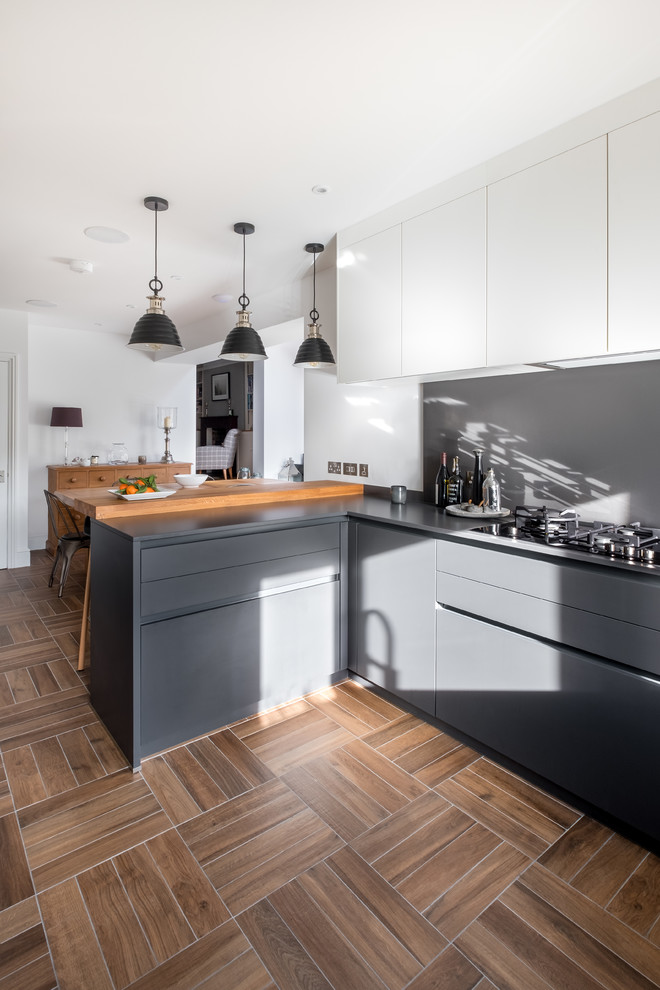 Medium sized contemporary u-shaped kitchen/diner in Gloucestershire with a submerged sink, glass-front cabinets, grey cabinets, quartz worktops, grey splashback, black appliances, porcelain flooring, a breakfast bar and brown floors.