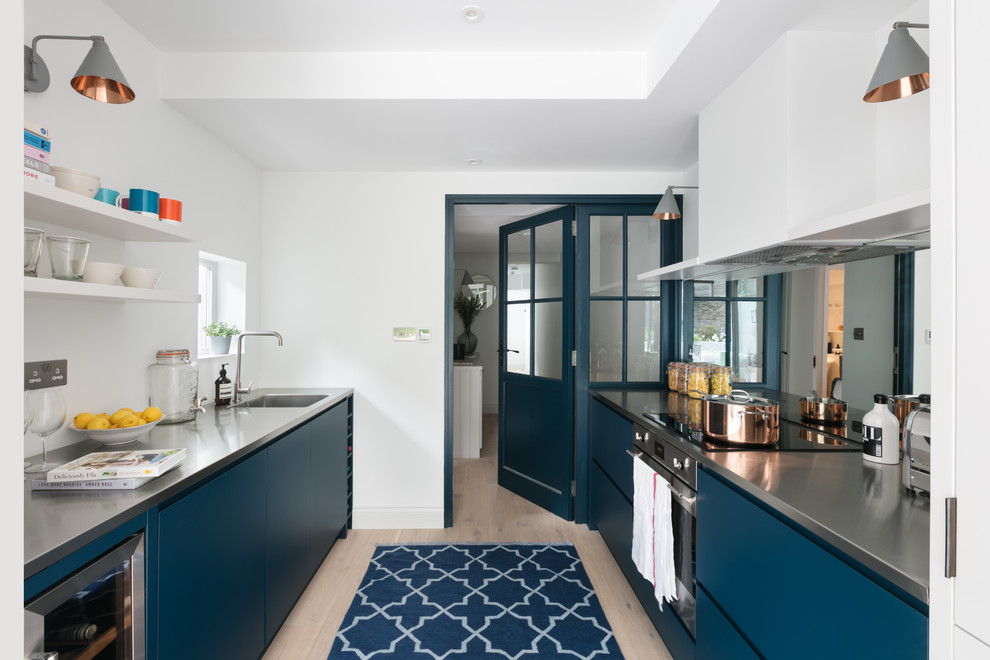 Modern inredning av ett kök, med en integrerad diskho, släta luckor, blå skåp, bänkskiva i rostfritt stål, ljust trägolv och beiget golv