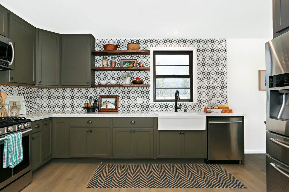 Inspiration for a mediterranean l-shaped medium tone wood floor kitchen remodel in Los Angeles with a farmhouse sink, recessed-panel cabinets, green cabinets, multicolored backsplash, stainless steel appliances, no island and cement tile backsplash