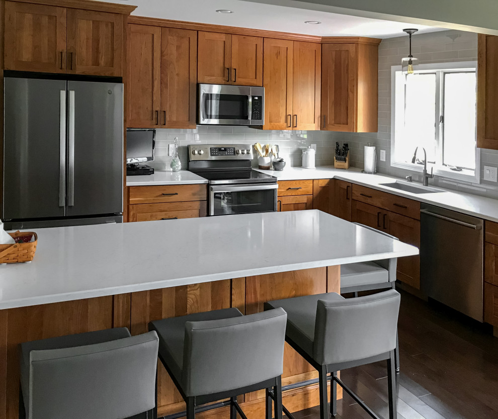 Small transitional l-shaped eat-in kitchen photo in New York with an undermount sink, shaker cabinets, medium tone wood cabinets, quartz countertops, gray backsplash, stainless steel appliances, an island and white countertops