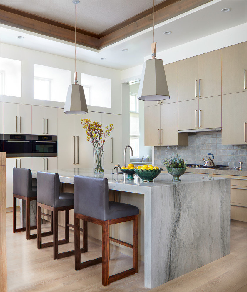 Kitchen - large contemporary light wood floor kitchen idea in Denver with flat-panel cabinets, stone tile backsplash, stainless steel appliances, an island, beige cabinets and gray backsplash