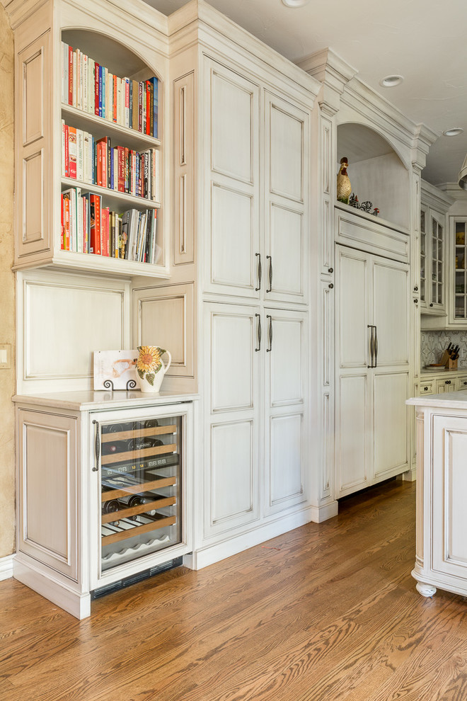 Bild på ett stort vit vitt kök, med en undermonterad diskho, luckor med upphöjd panel, skåp i slitet trä, bänkskiva i kvartsit, vitt stänkskydd, stänkskydd i keramik, integrerade vitvaror, ljust trägolv, en köksö och brunt golv