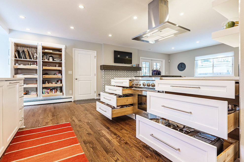 Foto på ett litet vintage vit kök, med en undermonterad diskho, skåp i shakerstil, vita skåp, bänkskiva i kvarts, brunt stänkskydd, stänkskydd i porslinskakel, rostfria vitvaror, mellanmörkt trägolv, en halv köksö och brunt golv