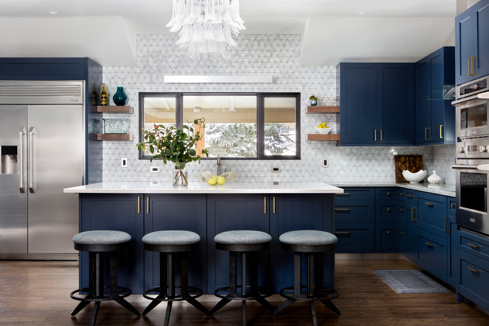 Foto på ett vintage vit l-kök, med skåp i shakerstil, blå skåp, vitt stänkskydd, rostfria vitvaror, mörkt trägolv, en köksö och brunt golv