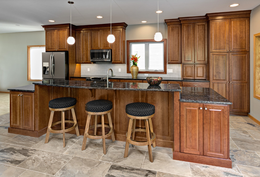 Inspiration for a large timeless galley porcelain tile and gray floor eat-in kitchen remodel in Minneapolis with a triple-bowl sink, raised-panel cabinets, medium tone wood cabinets, quartz countertops, gray backsplash, cement tile backsplash, stainless steel appliances, an island and gray countertops