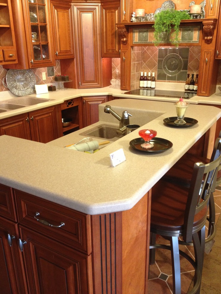 Photo of a medium sized classic l-shaped enclosed kitchen in Philadelphia with a triple-bowl sink, raised-panel cabinets, medium wood cabinets, laminate countertops, brown splashback, ceramic splashback, stainless steel appliances, travertine flooring and an island.