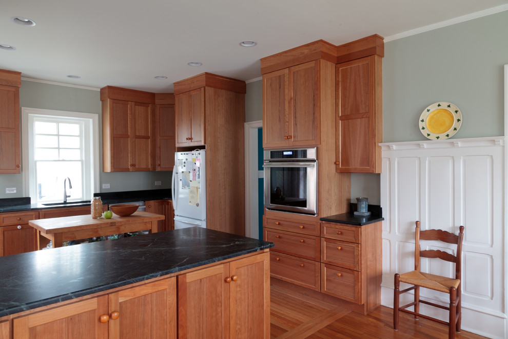 Idéer för ett mellanstort amerikanskt kök, med en undermonterad diskho, luckor med infälld panel, bruna skåp, bänkskiva i täljsten, rostfria vitvaror, ljust trägolv, en halv köksö och brunt golv