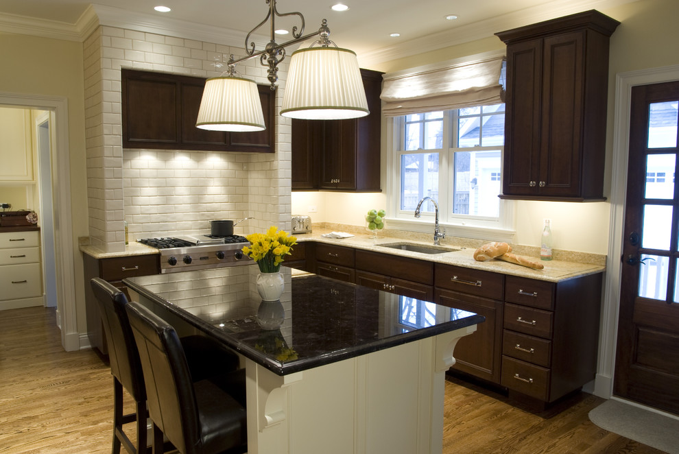 Klassisk inredning av ett kök, med en undermonterad diskho, luckor med infälld panel, skåp i mörkt trä, granitbänkskiva, vitt stänkskydd, stänkskydd i tunnelbanekakel och rostfria vitvaror