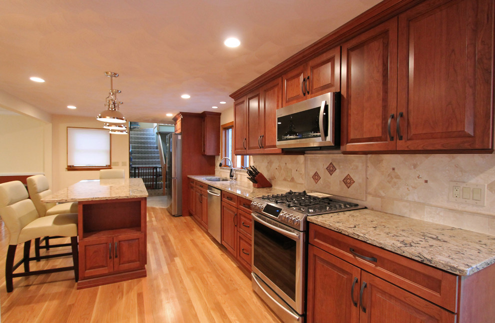 Exempel på ett mellanstort klassiskt kök och matrum, med en undermonterad diskho, luckor med upphöjd panel, skåp i mellenmörkt trä, bänkskiva i kvarts, beige stänkskydd, stänkskydd i sten, rostfria vitvaror, ljust trägolv och en köksö