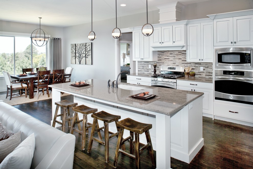 Large traditional galley kitchen/diner in Salt Lake City with a submerged sink, raised-panel cabinets, white cabinets, engineered stone countertops, multi-coloured splashback, stone tiled splashback, stainless steel appliances, dark hardwood flooring and an island.
