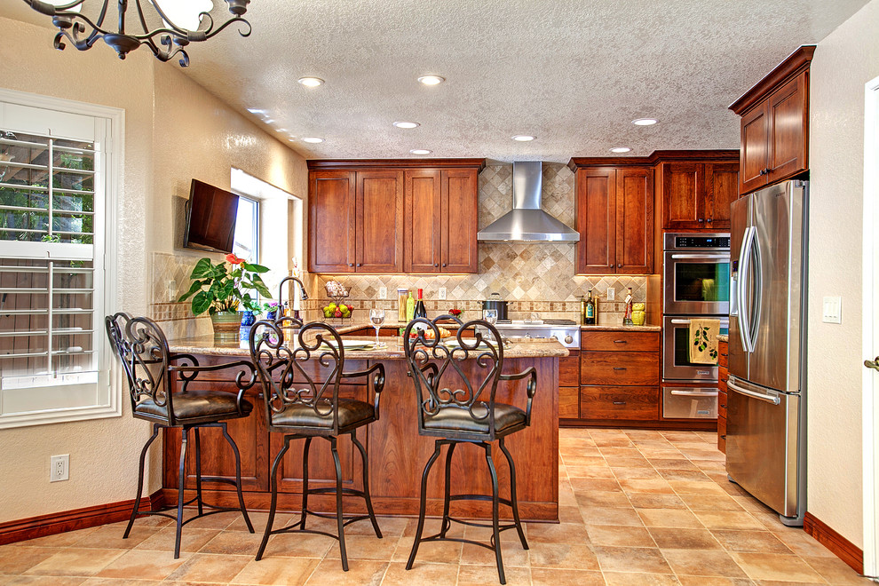 Large mountain style u-shaped porcelain tile eat-in kitchen photo in San Diego with a peninsula, recessed-panel cabinets, medium tone wood cabinets, granite countertops, beige backsplash, stone tile backsplash, stainless steel appliances and an undermount sink