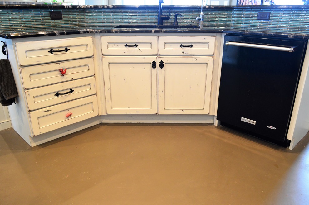 Foto på ett mellanstort lantligt u-kök, med luckor med infälld panel, skåp i slitet trä, granitbänkskiva, blått stänkskydd, stänkskydd i keramik, svarta vitvaror, betonggolv, en köksö och brunt golv