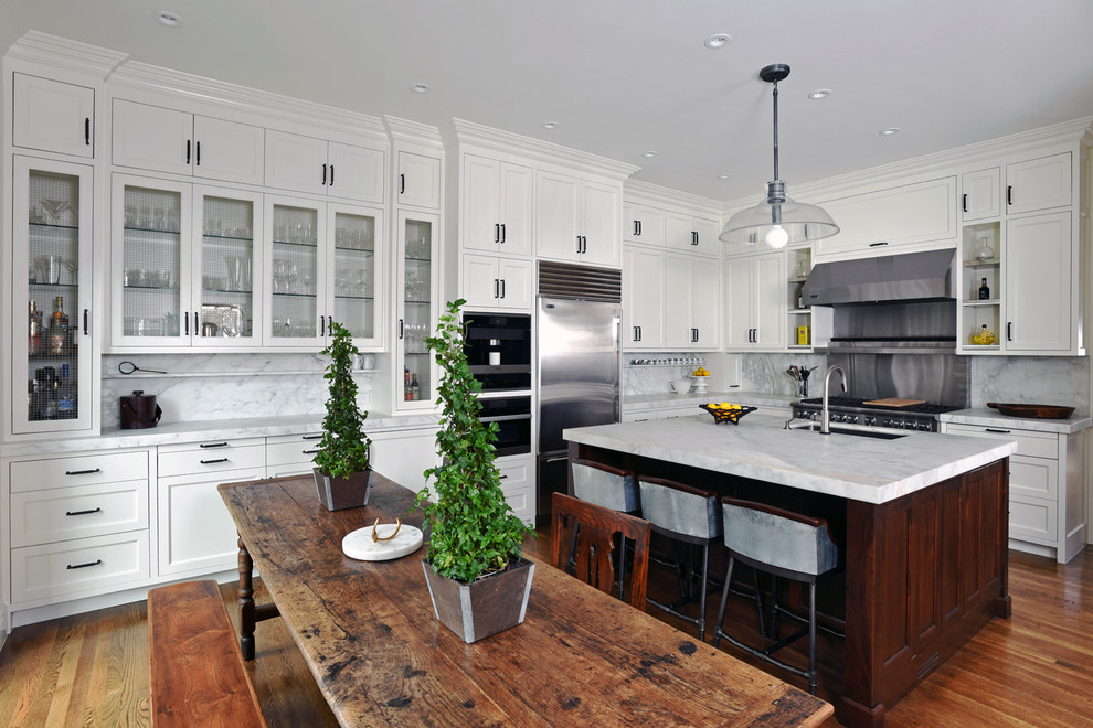 Inredning av ett klassiskt mellanstort kök, med en undermonterad diskho, luckor med infälld panel, vita skåp, marmorbänkskiva, vitt stänkskydd, stänkskydd i marmor, rostfria vitvaror, mörkt trägolv, en köksö och brunt golv