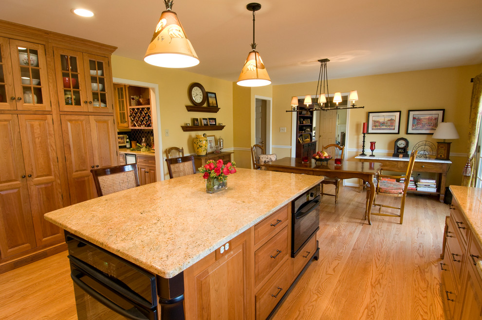 Example of a classic light wood floor eat-in kitchen design in Philadelphia with an undermount sink, raised-panel cabinets, medium tone wood cabinets, granite countertops, black appliances, an island and beige backsplash
