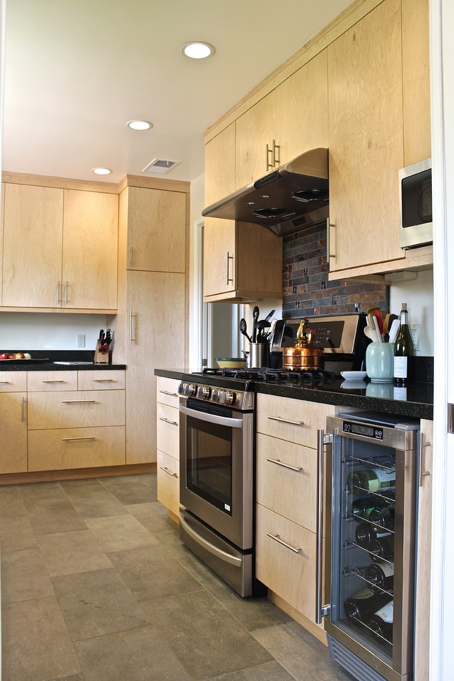 Exemple d'une petite cuisine moderne en L et bois clair fermée avec un évier encastré, un placard à porte plane, un plan de travail en granite, une crédence noire, une crédence en ardoise, un électroménager en acier inoxydable et carreaux de ciment au sol.