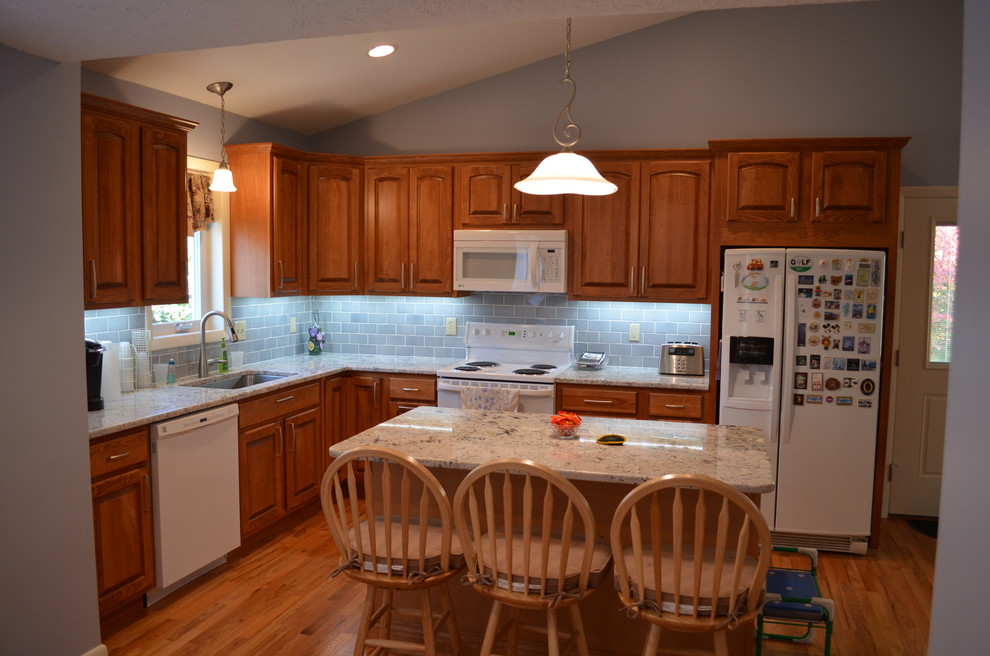 Inspiration for a mid-sized timeless l-shaped light wood floor open concept kitchen remodel in Bridgeport with a single-bowl sink, raised-panel cabinets, medium tone wood cabinets, laminate countertops, blue backsplash, ceramic backsplash and white appliances