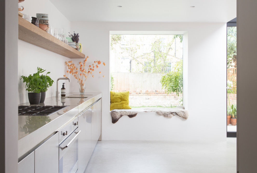 ロンドンにある高級な中くらいな北欧スタイルのおしゃれなI型キッチン (一体型シンク、フラットパネル扉のキャビネット、シルバーの調理設備、アイランドなし、白いキャビネット、コンクリートの床) の写真