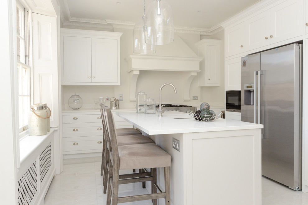 Inspiration for a coastal kitchen in London with shaker cabinets, white cabinets, white splashback, stainless steel appliances, an island, white floors and white worktops.