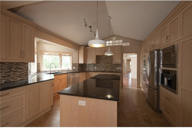 This is an example of a large classic kitchen in Calgary with granite worktops, multi-coloured splashback, mosaic tiled splashback, stainless steel appliances, an island, a submerged sink, flat-panel cabinets, light wood cabinets and porcelain flooring.