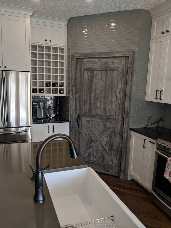 Photo of a medium sized contemporary l-shaped kitchen pantry in Calgary with a belfast sink, shaker cabinets, white cabinets, composite countertops, grey splashback, metro tiled splashback, stainless steel appliances, medium hardwood flooring, an island, brown floors and grey worktops.