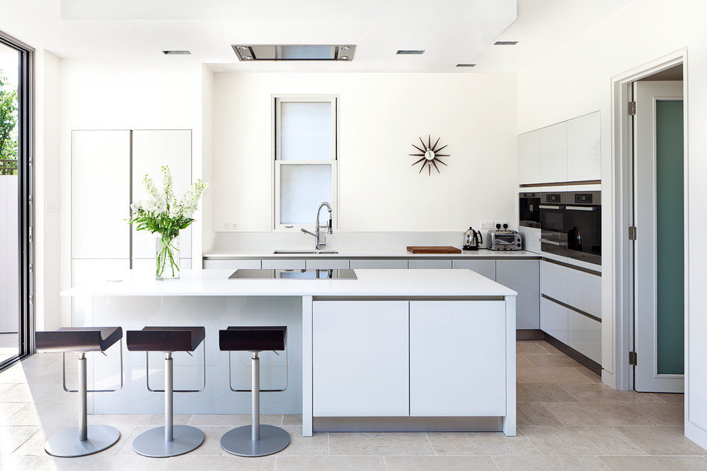 Стильный дизайн: угловая кухня в современном стиле с врезной мойкой, плоскими фасадами, белыми фасадами, белым фартуком, островом и бежевым полом - последний тренд