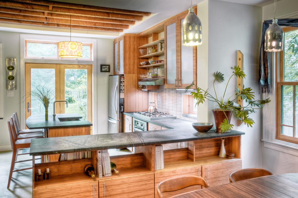 Foto på ett funkis kök, med rostfria vitvaror, luckor med glaspanel, skåp i mellenmörkt trä och bänkskiva i täljsten