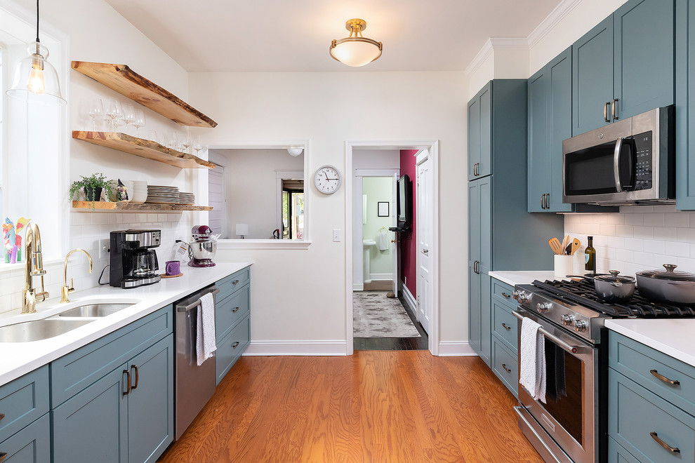 Traditional galley enclosed kitchen in Philadelphia with a submerged sink, shaker cabinets, blue cabinets, white splashback, metro tiled splashback, stainless steel appliances, medium hardwood flooring, brown floors and white worktops.