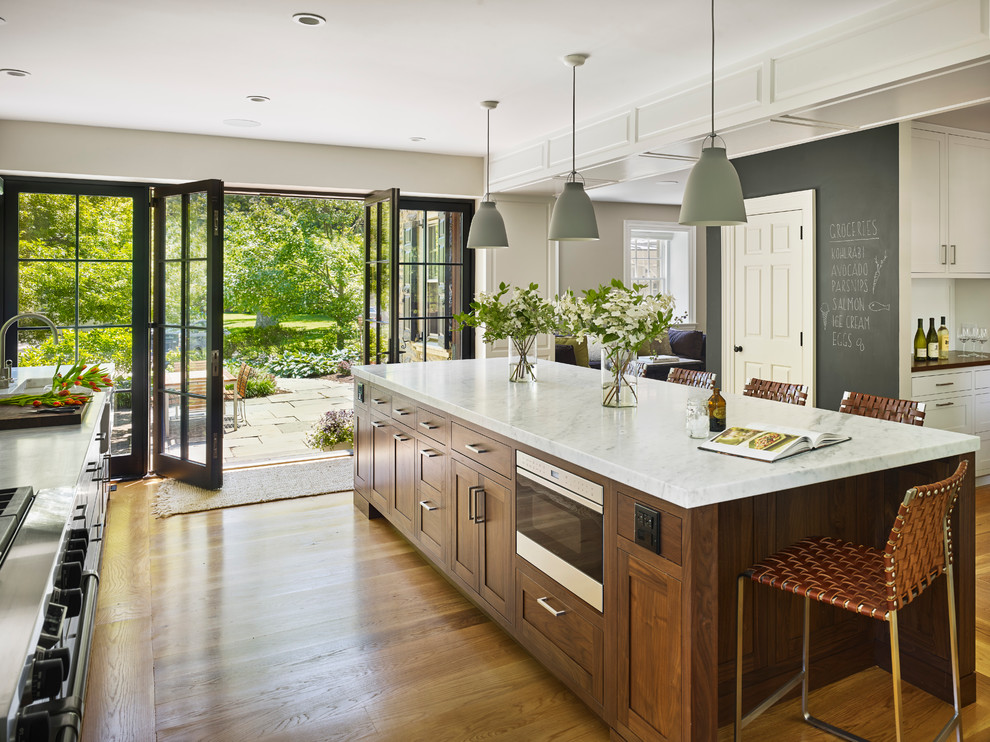 Inspiration for a large transitional l-shaped light wood floor kitchen remodel in Philadelphia with a farmhouse sink, shaker cabinets, dark wood cabinets, marble countertops, white backsplash, ceramic backsplash, paneled appliances and an island