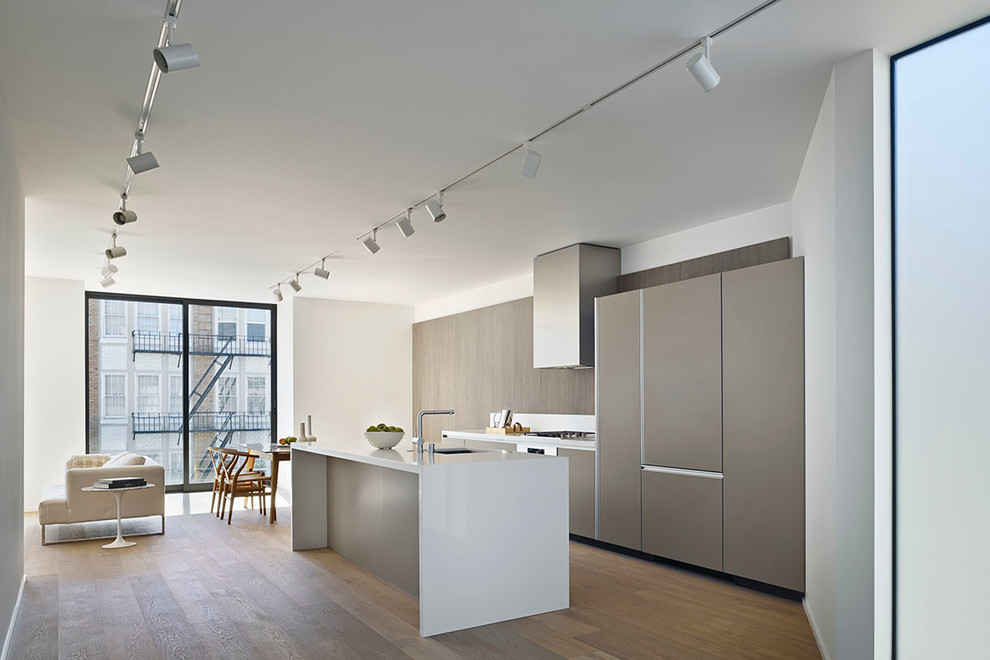 Inspiration for a medium sized contemporary galley open plan kitchen in San Francisco with a submerged sink, flat-panel cabinets, grey cabinets, quartz worktops, white splashback, stone slab splashback, integrated appliances, light hardwood flooring and an island.