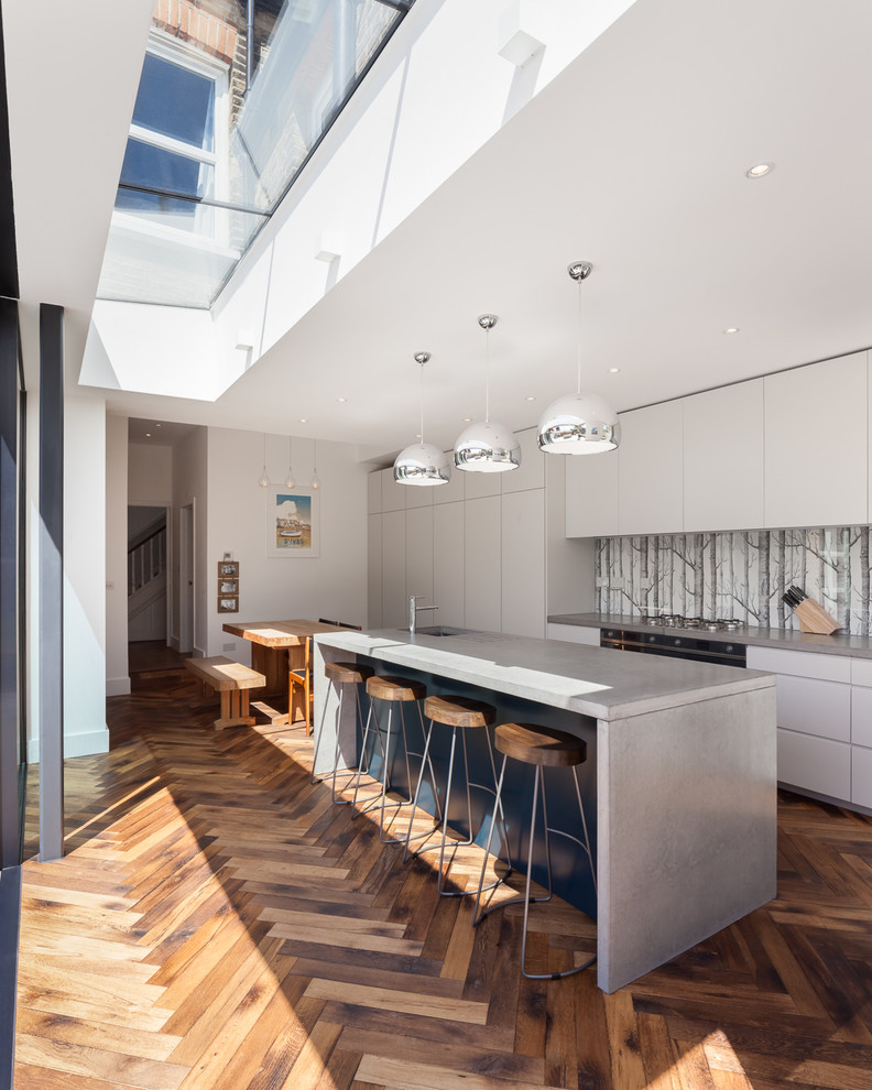 Eat-in kitchen - contemporary medium tone wood floor and brown floor eat-in kitchen idea in London with flat-panel cabinets, concrete countertops, gray backsplash and an island