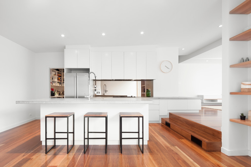 Zweizeilige, Große Moderne Küche mit flächenbündigen Schrankfronten, weißen Schränken, Küchengeräten aus Edelstahl, braunem Holzboden und Kücheninsel in Melbourne